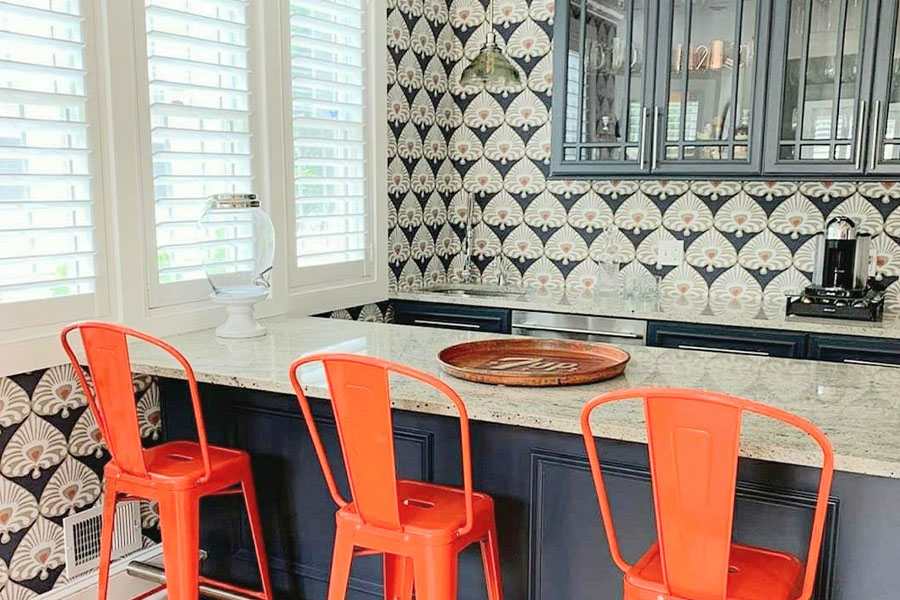 Bright orange bar stools with vibrant design wallpaper in a kitchen.